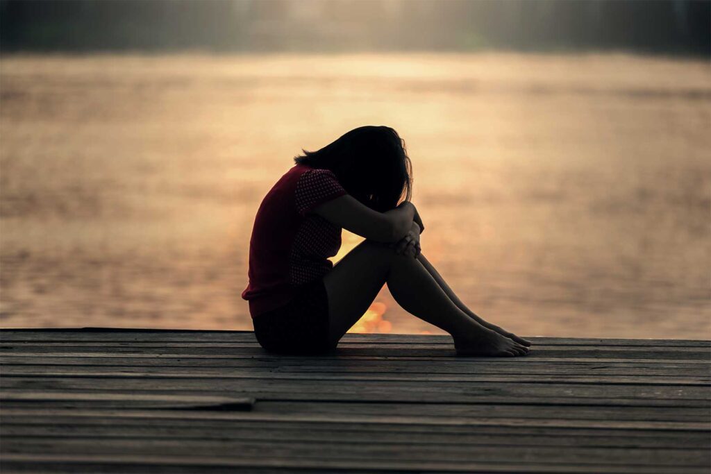 a woman sitting on a dock with her head in her hands