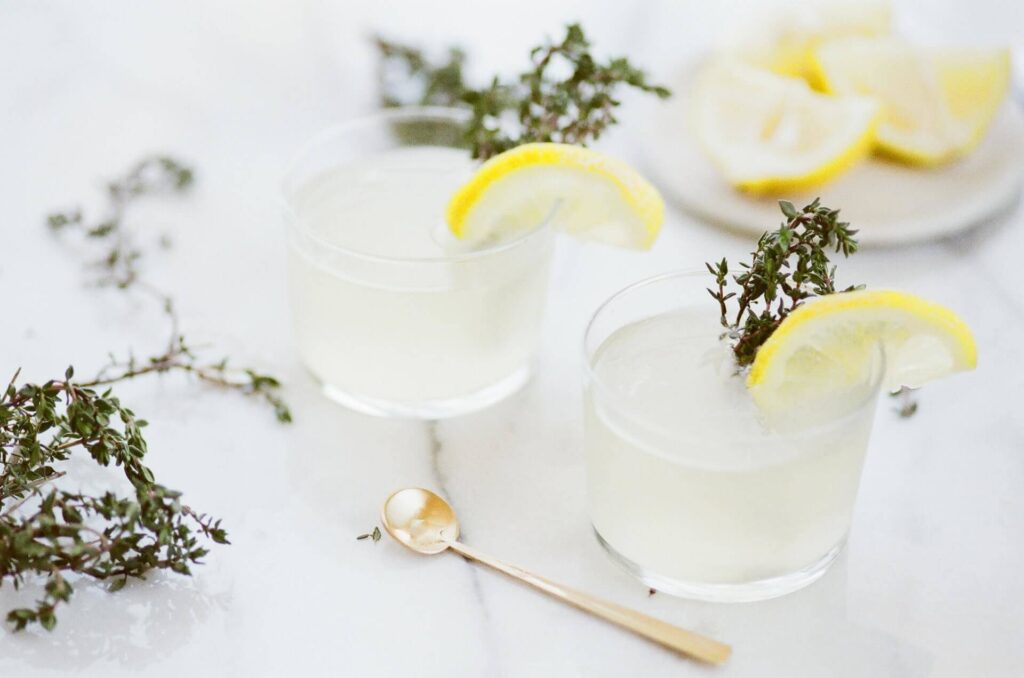 two glasses of liquid with lemon slices and a lemon on top