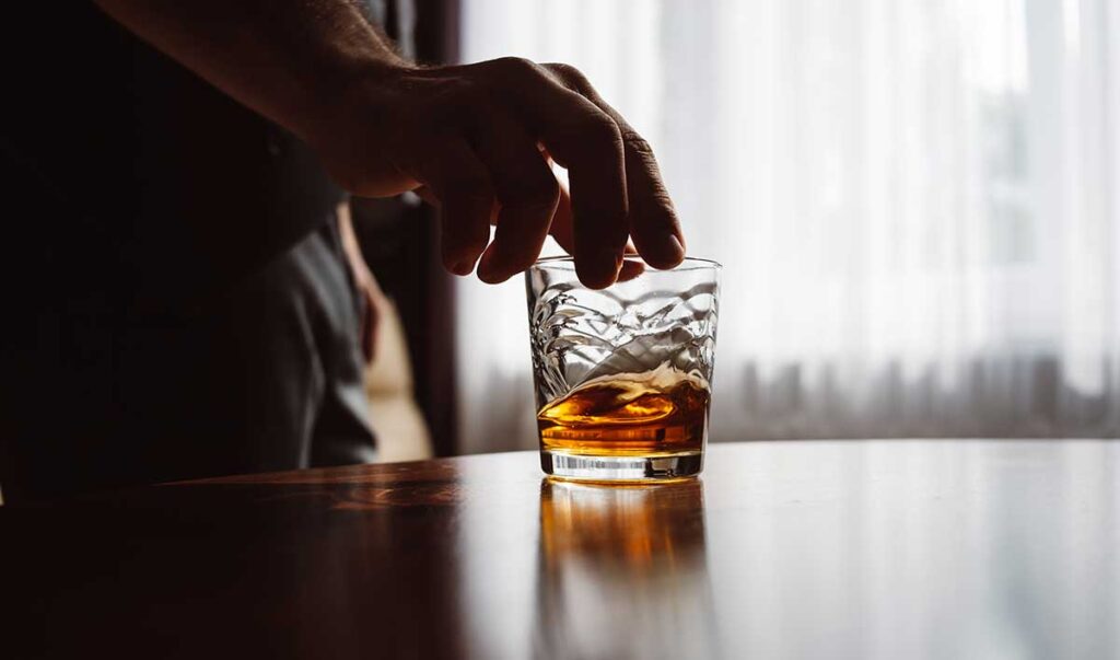 a hand holding a glass of amber liquid